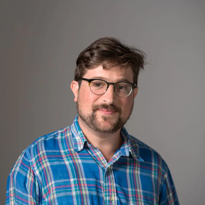 Studio portrait of Hans Kulla-Mader wearing glasses and a blue plaid shirt
