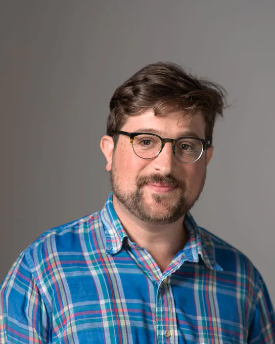 Studio portrait of Hans Kulla-Mader wearing glasses and a blue plaid shirt